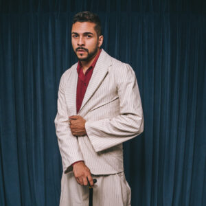 Carlos Veloso de terno claro e camisa vermelha, segurando uma bengala