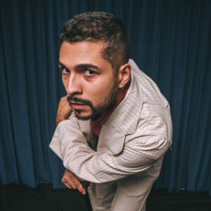 Carlos Veloso de terno claro e camisa vermelha, segurando uma bengala