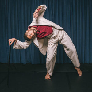 Carlos Veloso de terno claro e camisa vermelha, segurando uma bengala